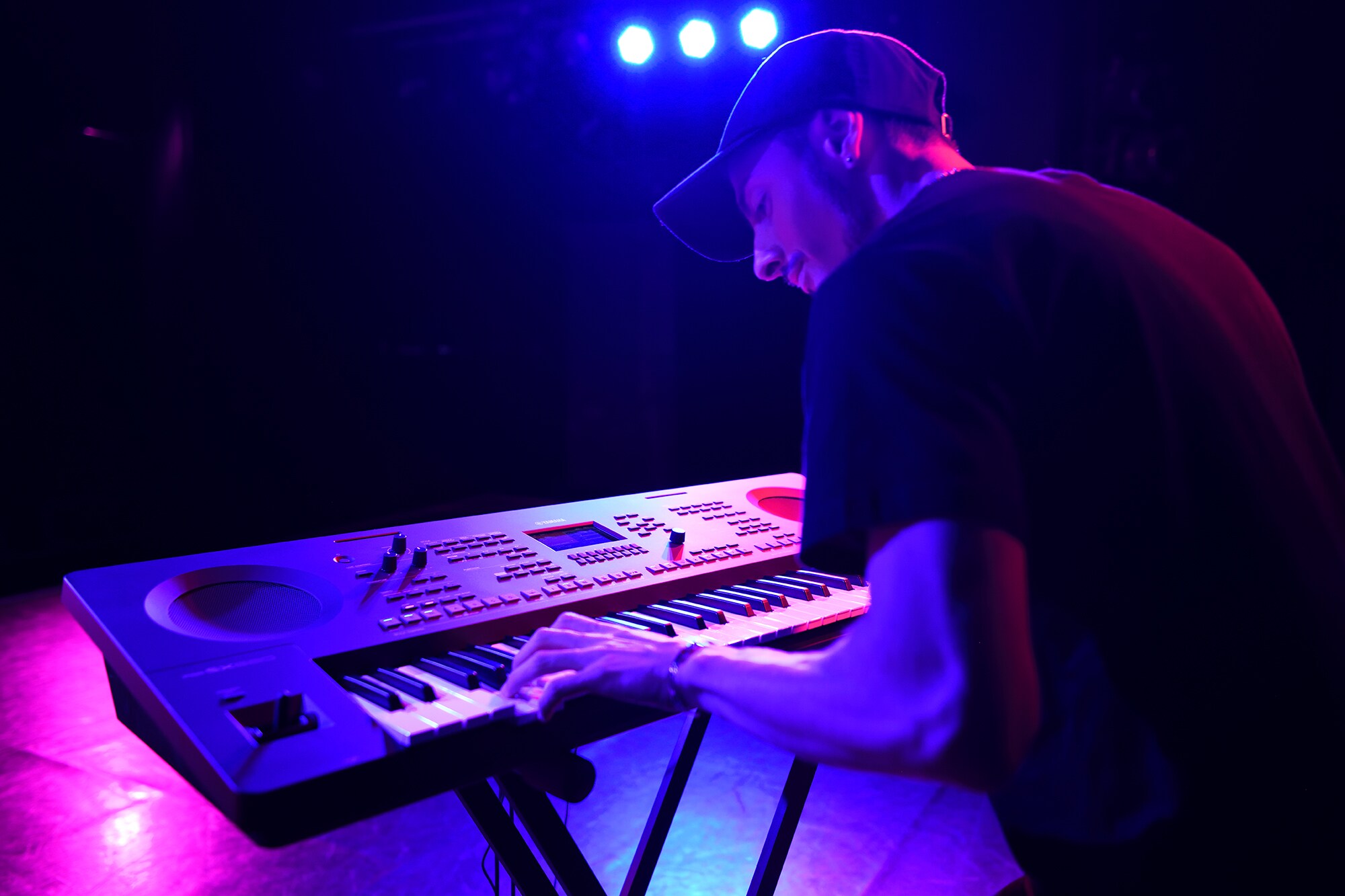 A person playing a Yamaha arranger workstation on a stand under stage lighting